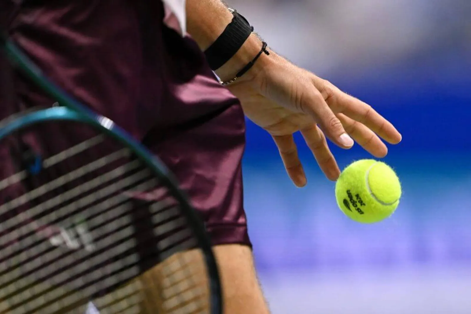 A close-up of Alexander Zverev's left hand releasing a ball to bounce it on his serve, with his racket and shorts visible.