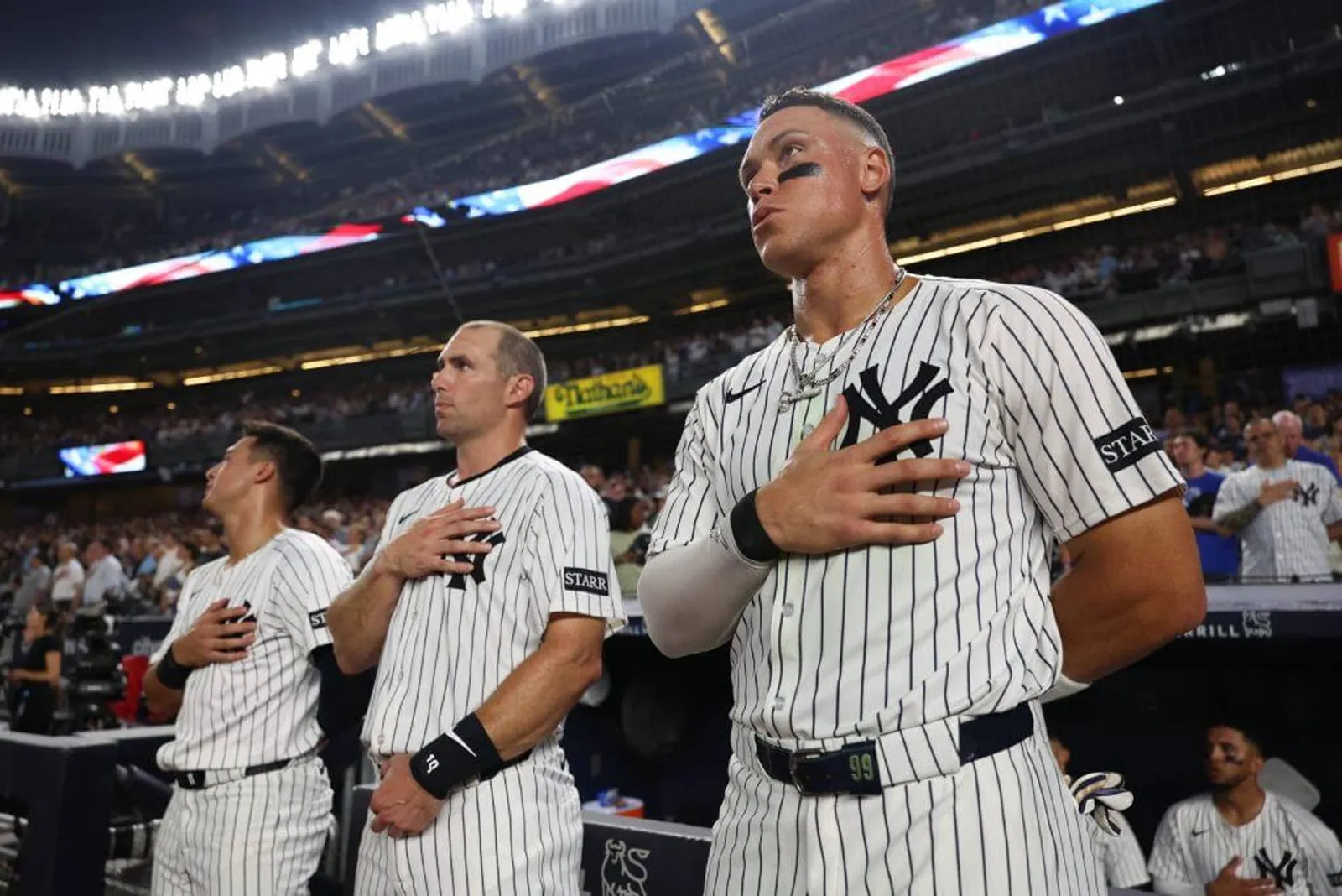 Aaron Judge, Paul Goldschmidt and Anthony Volpe stand as "God Bless America" is played at a Yankees game in 2025.