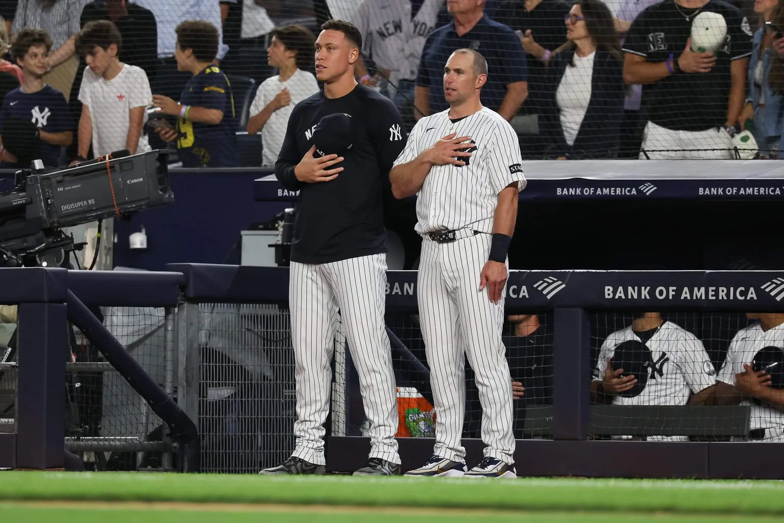 Paul Goldschmidt, right, with pinstriped jersey top and pants, and Aaron Judge, with dark pullover and pinstriped pants, stand just outside a dugout.